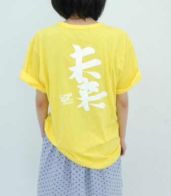 Bright yellow T-shirt featuring bold white Japanese characters by Yoshitomo Nara and Satoshi Ohno.