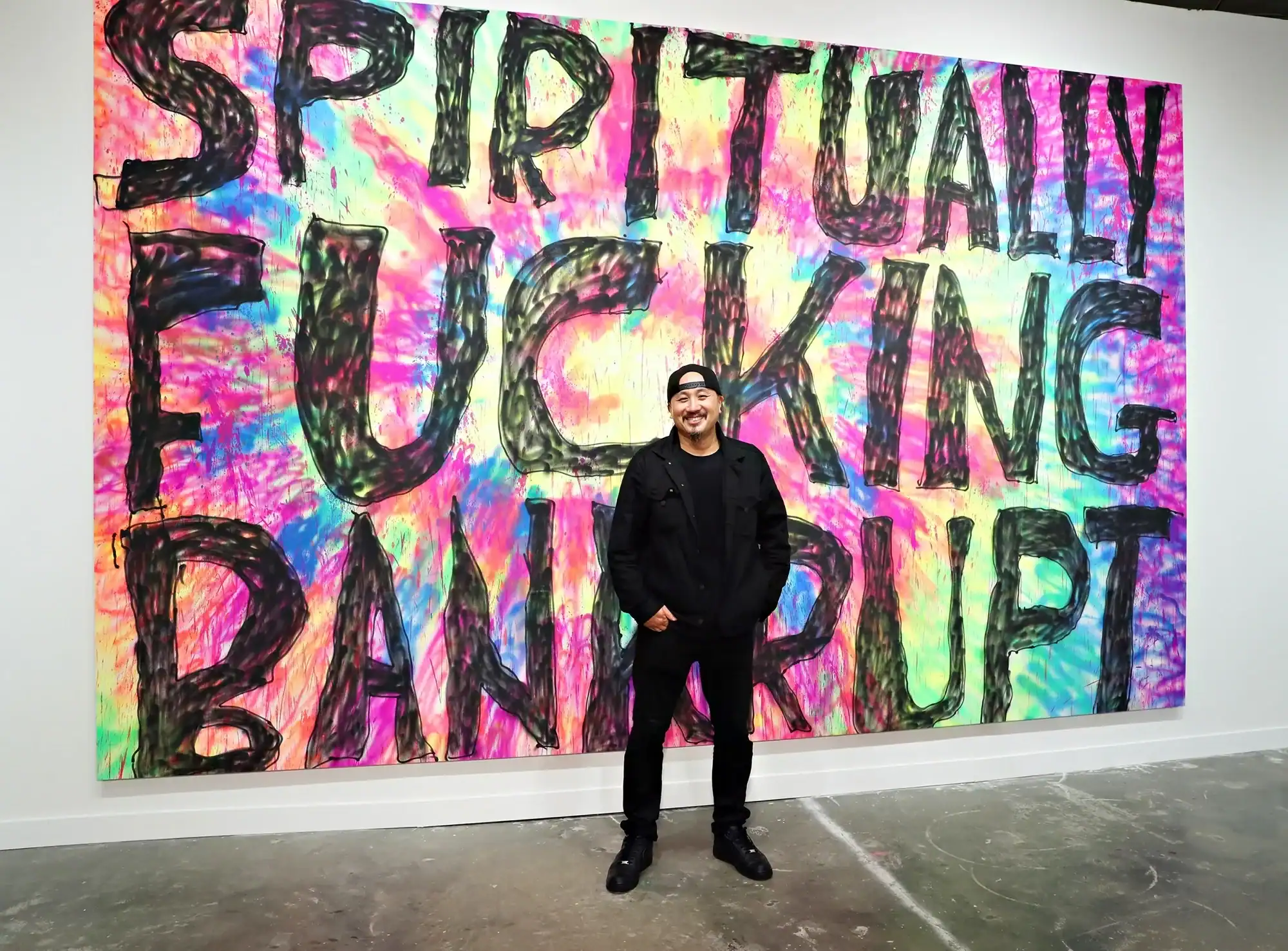 Man standing in front of colorful graffiti wall with bold "Spiritually F***ing Banned" message.