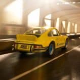 Porsche 911 toy car in yellow with blue wheels, driving through an urban tunnel at night.