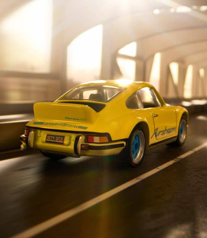 Porsche 911 model toy car on city street at night Porsche 911 toy car in yellow with blue wheels, driving through an urban tunnel at night.